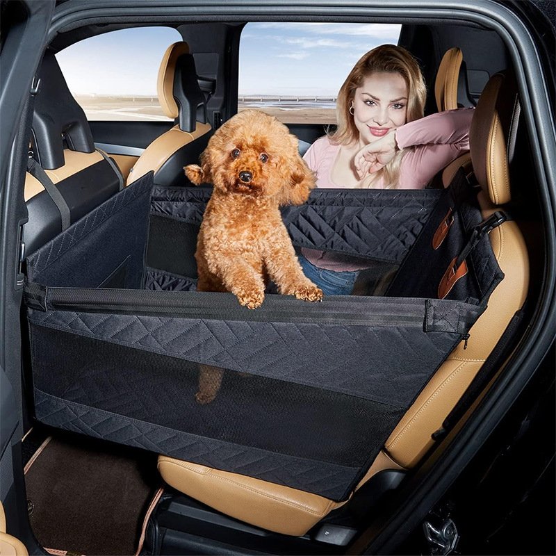 A dog sitting comfortably on a waterproof hammock-style car seat protector during a road trip.